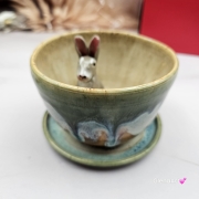 Filiżanka ZAJĄC ceramiczna ze spodkiem z ZAJĄCEM szarakiem w środku ręcznie toczona i malowana w kolorach zielonych niebieskich brązach i beżach oraz szary zając kubek zając z zającem szarakiem filiżanka na Wielkanoc i nie tylko